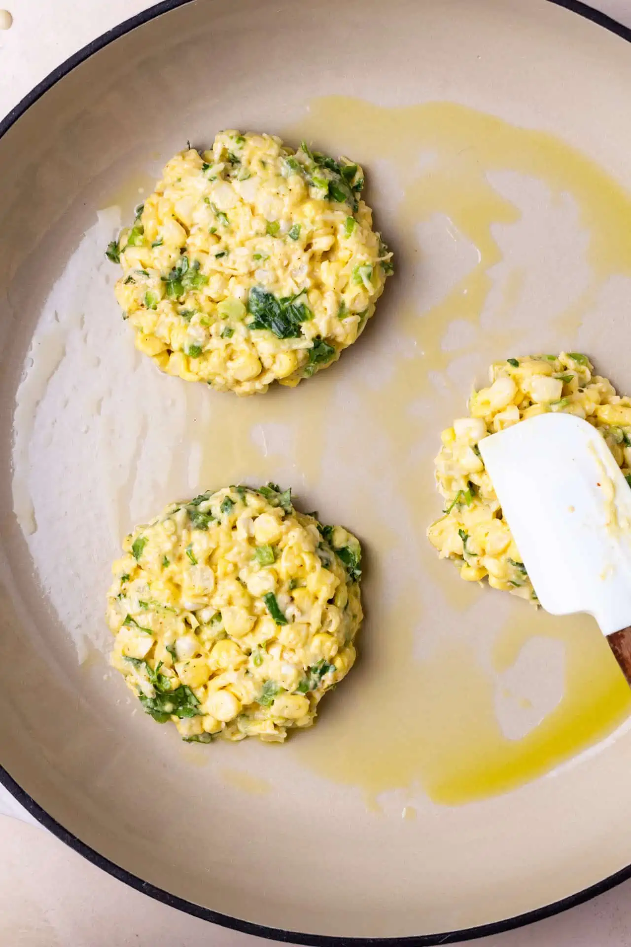Frying up corn fritters in a skillet with extra virgin olive oil.