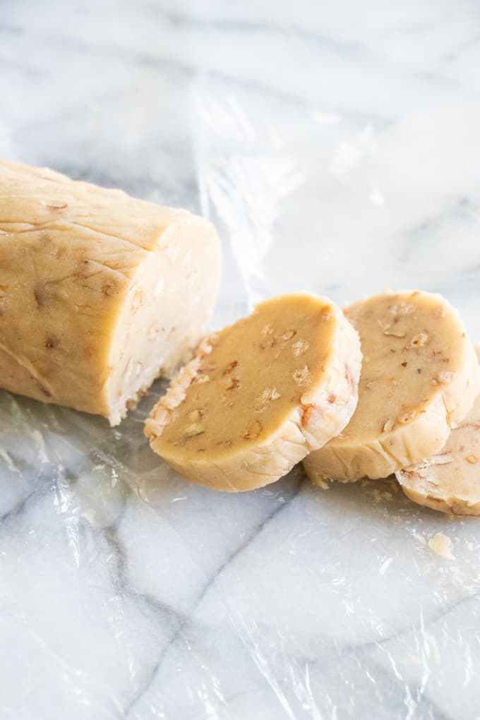 A roll of butter pecan shortbread cookies and slices being cut off to form into cookies.