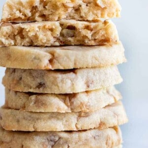 A stack of butter pecan shortbread cookies with bits of pecans and toffee bits around.