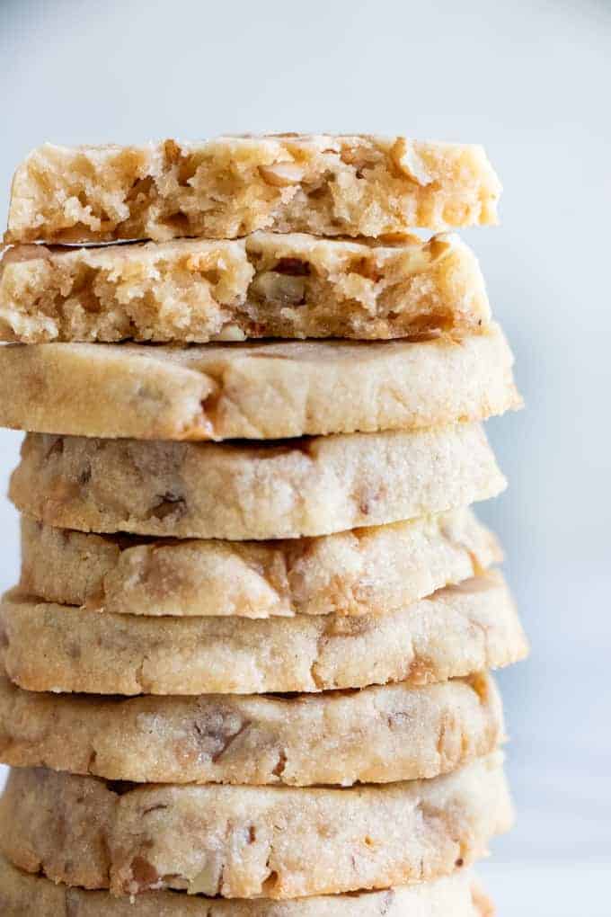 A stack of butter pecan shortbread cookies with bits of pecans and toffee bits around.