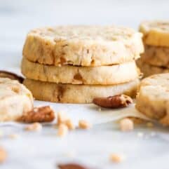 A stack of butter pecan shortbread cookies with bits of pecans and toffee bits around.