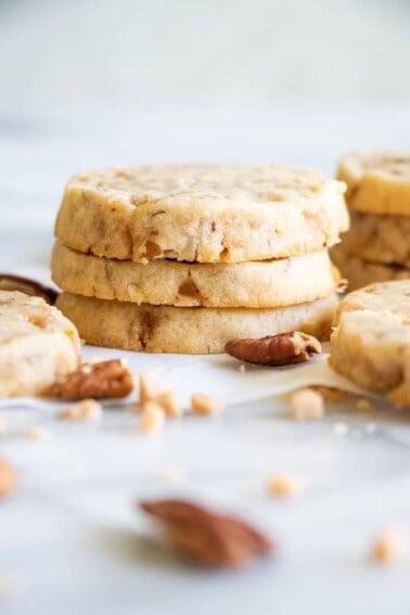 A stack of butter pecan shortbread cookies with bits of pecans and toffee bits around.
