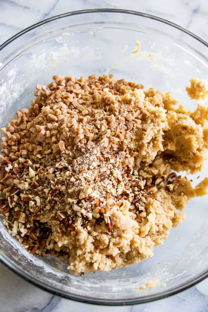 Bowl filled with butter pecan shortbread cookie dough topped with bits of chopped pecans and toffee bits.