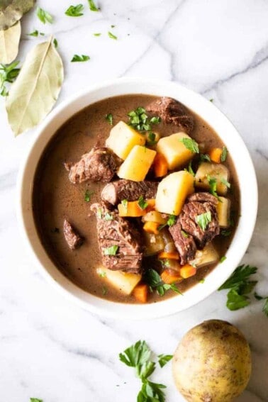 A bowl filled with beef stew, tender meat, flavorful gravy broth. Topped with fresh parsley.