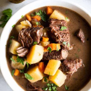 A bowl filled with beef stew, tender meat, flavorful gravy broth. Topped with fresh parsley.