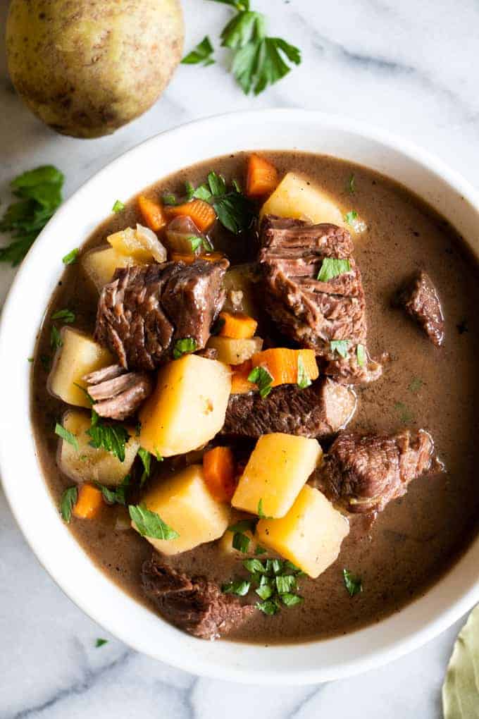 A bowl filled with beef stew, tender meat, flavorful gravy broth. Topped with fresh parsley.