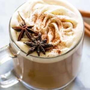 A glass mug filled with apple spice latte, topped with whipped cream and star anise for decoration.