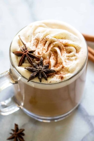 A glass mug filled with apple spice latte, topped with whipped cream and star anise for decoration.