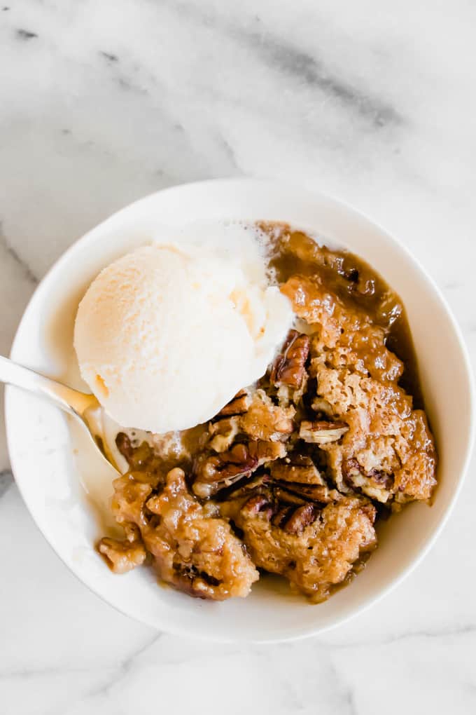 A bowl filled with pecan cobbler and a scoop of vanilla ice cream on top.