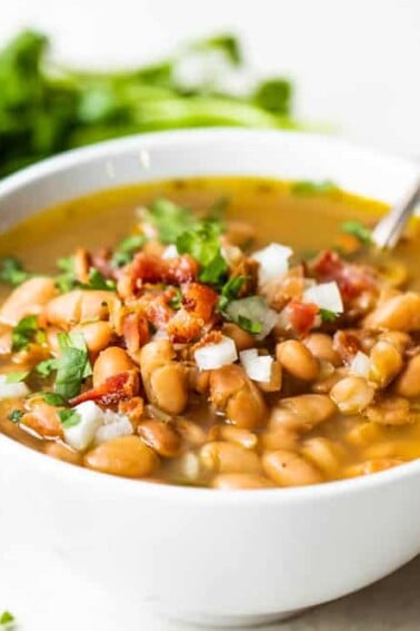 Bowl of charro beans served with a spoon.