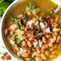 Overhead view of charro beans topped with crisp bacon and diced onion.