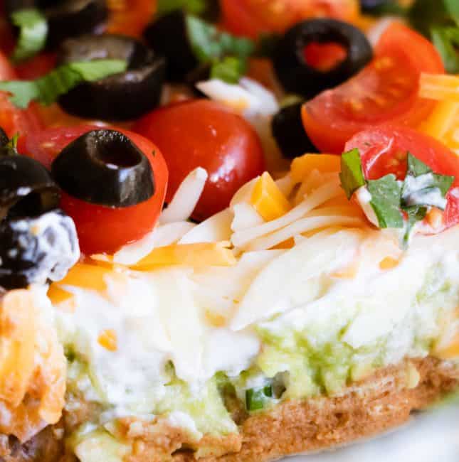 7 layer dip showing refried beans, guacamole, sour cream, cheese, tomato, olives and green onion.