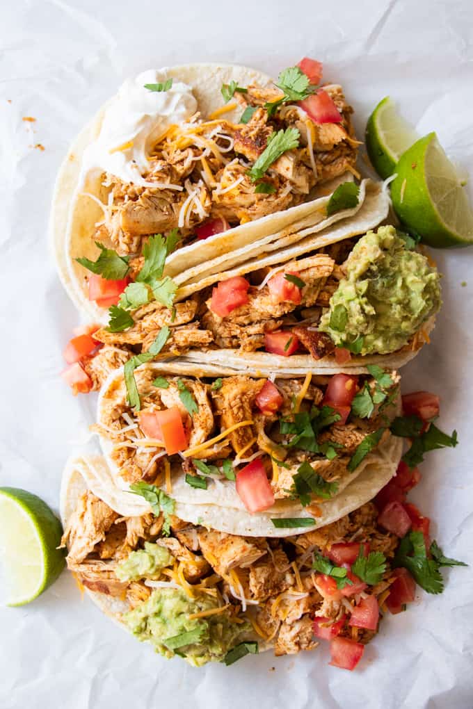 A tray filled with the best ever chicken tacos topped with scoops of guacamole, sour cream and diced tomatoes.