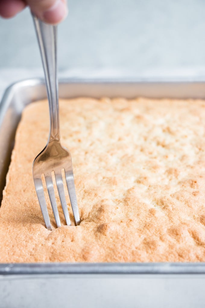 A fork poking holes into the top of the baked cake for tres leches cake.