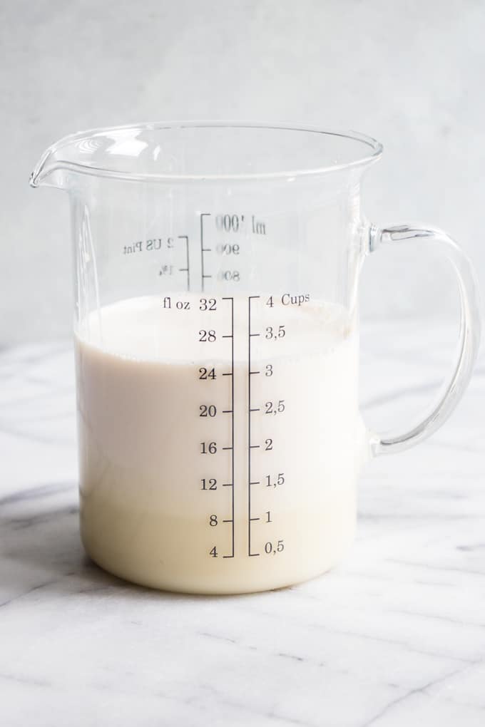 A measuring cup filled with three kinds of milk for a tres leches cake.