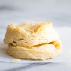 A homemade biscuit split in half, and stacked, with butter dripping out of the middle.