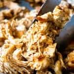 Tongs picking up shredded Mexican Chicken from a large skillet.
