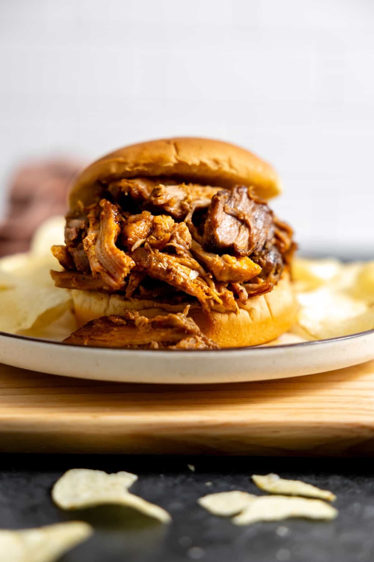 Slow cooker pulled pork on a hamburger bun served with potato chips.