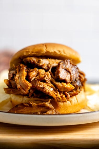 Slow cooker pulled pork on a hamburger bun served with potato chips.