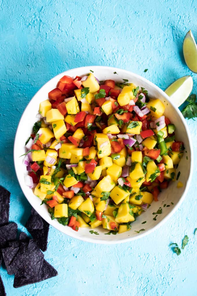 A bowl filled with freshly made mango salsa, tortilla chips and lime wedges. 