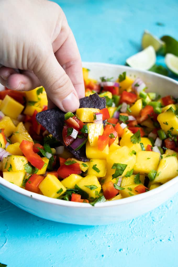 A blue tortilla chip digging into fresh mango salsa.