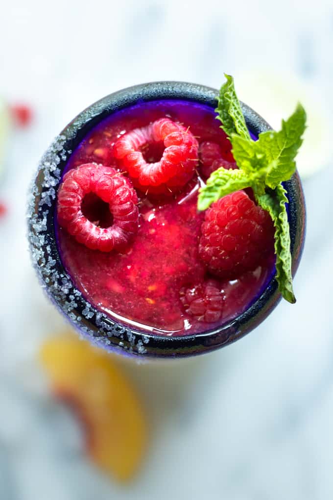 Overhead shot of a peach raspberry margarita topped with fresh raspberries and a sprig of mint.