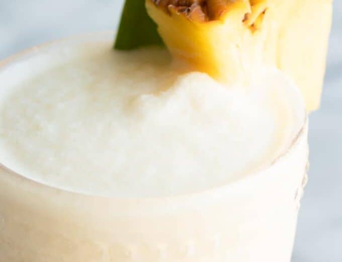 Up close of cold and frosty Pina coladas with a wedge of pineapple.