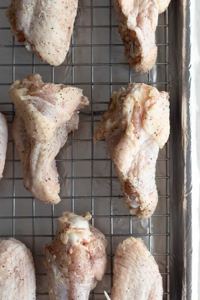 Chicken wings spread out on a wire rack over a baking sheet ready to bake and make chili lime chicken wings.