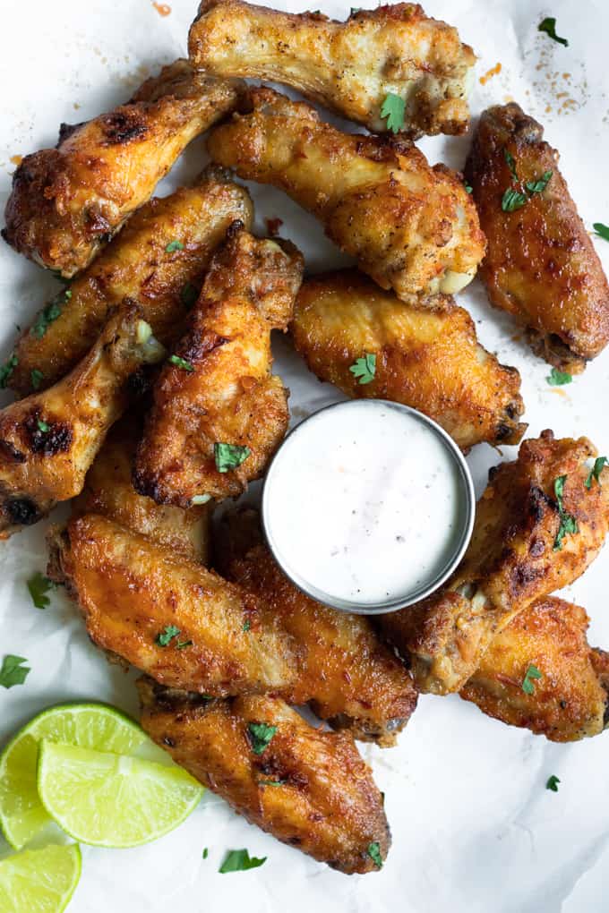 Chile Lime Chicken wings stacked around a cup of ranch, sprinkled with a garnish of cilantro and lime wedges.