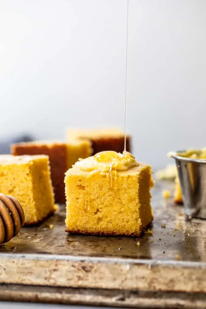 Slices of cornbread being served with butter and a drizzle of honey. 