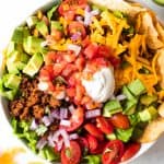 Taco salad showing all the toppings, ground taco meat, avocado, tomatoes, cheese, sour cream, salsa and tortilla chips.