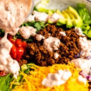 Dressing being drizzled on taco salad.