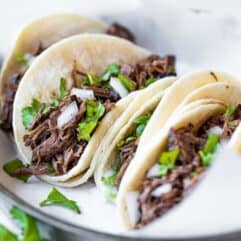 Slow cooker barbacoa loaded into white corn tortillas for street tacos.