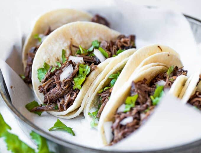 Slow cooker barbacoa loaded into white corn tortillas for street tacos.
