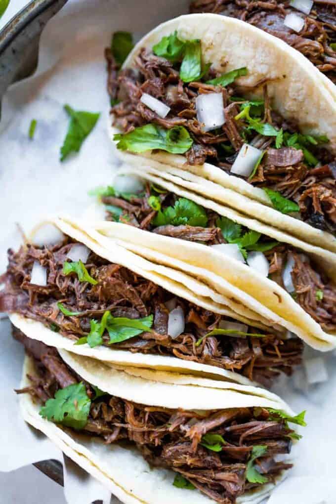 Slowcooker barbacoa straattaco's op een rij en belegd met koriander en blokjes ui.