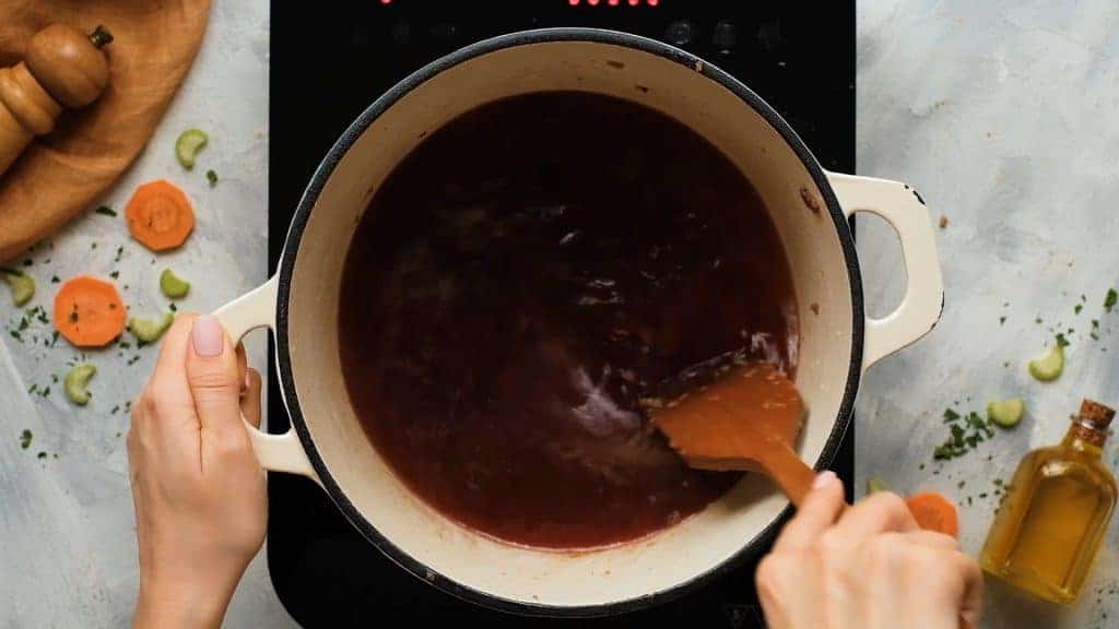 Stirring broth and wine in a dutch oven to deglaze and make broth for beef stew. 