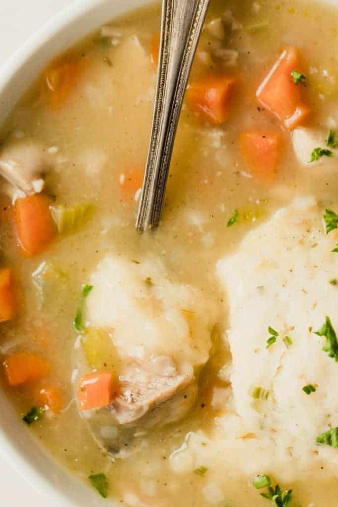 Up close view of a spoon with a chunk of dumpling, chicken and carrots in a golden broth.