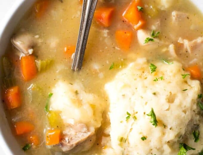 A bowl of chicken and dumplings, with a spoon digging in.