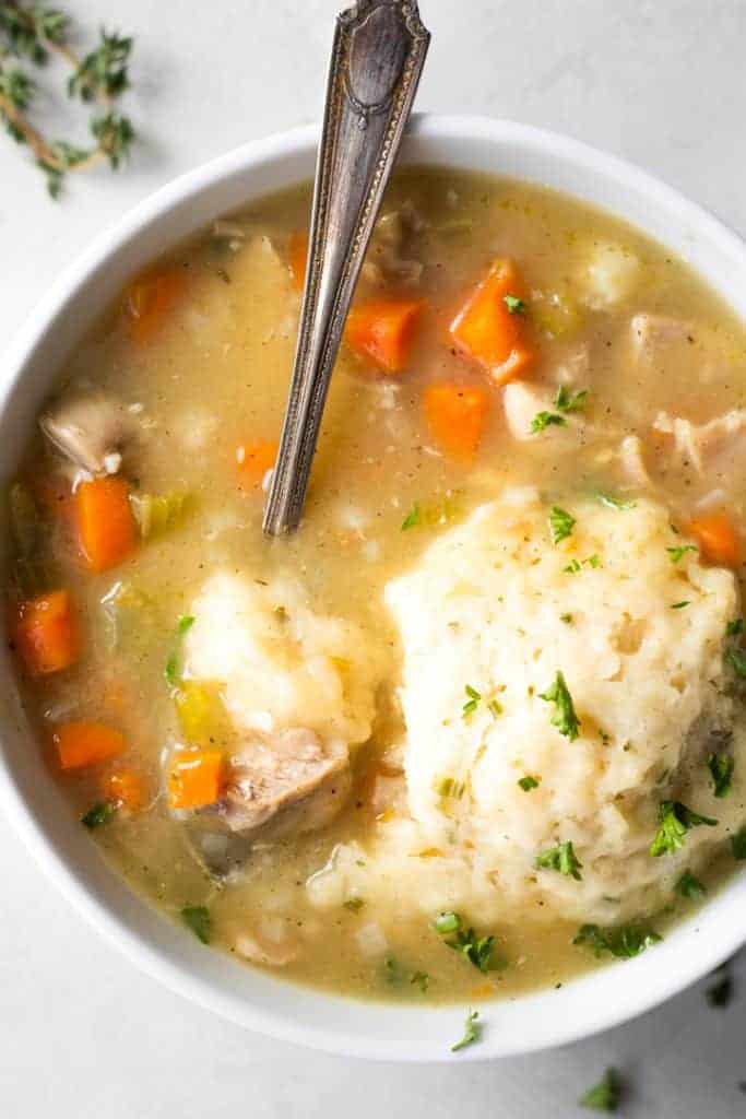 A bowl of chicken and dumplings, with a spoon digging in. 