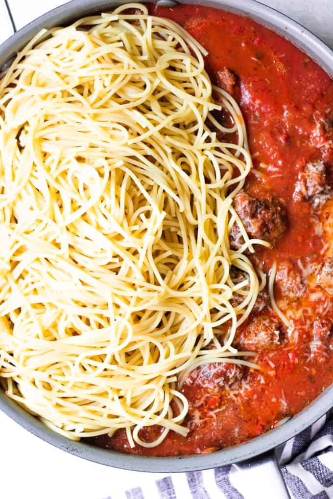 Skillet filled with homemade spaghetti sauce and meatballs mixing in spaghetti noodles.