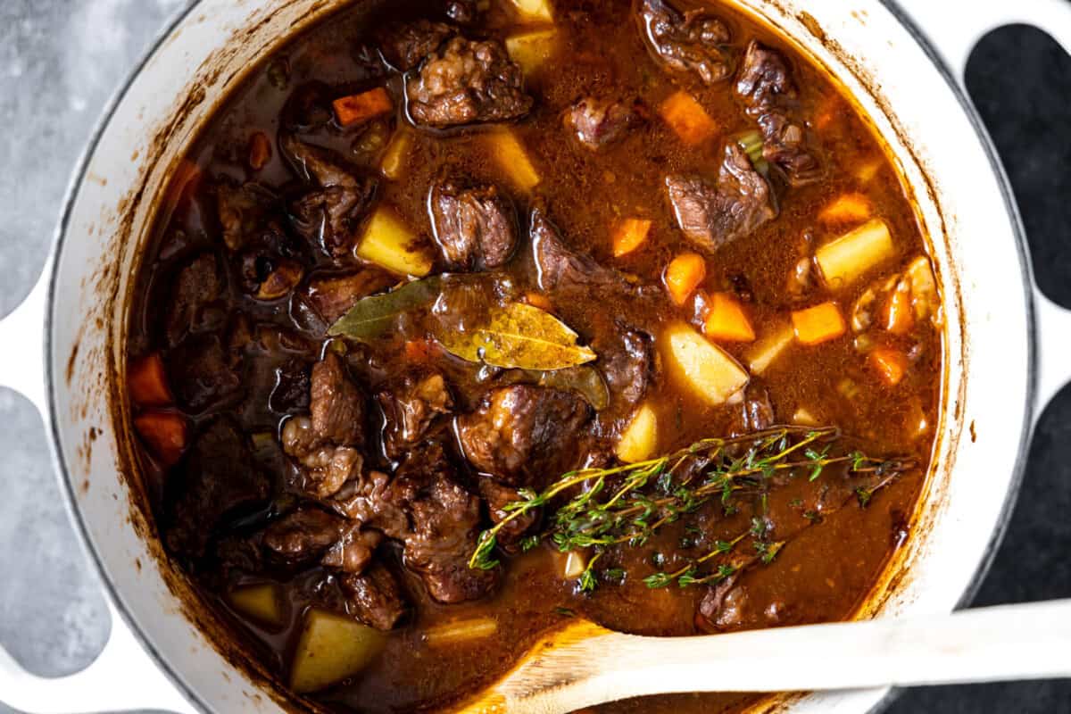 Beef stew in a large dutch oven with bayleaves and fresh thyme.