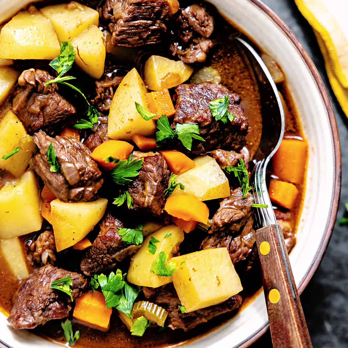 Beef stew with potatoes and carrots served in a bowl with a spoon.