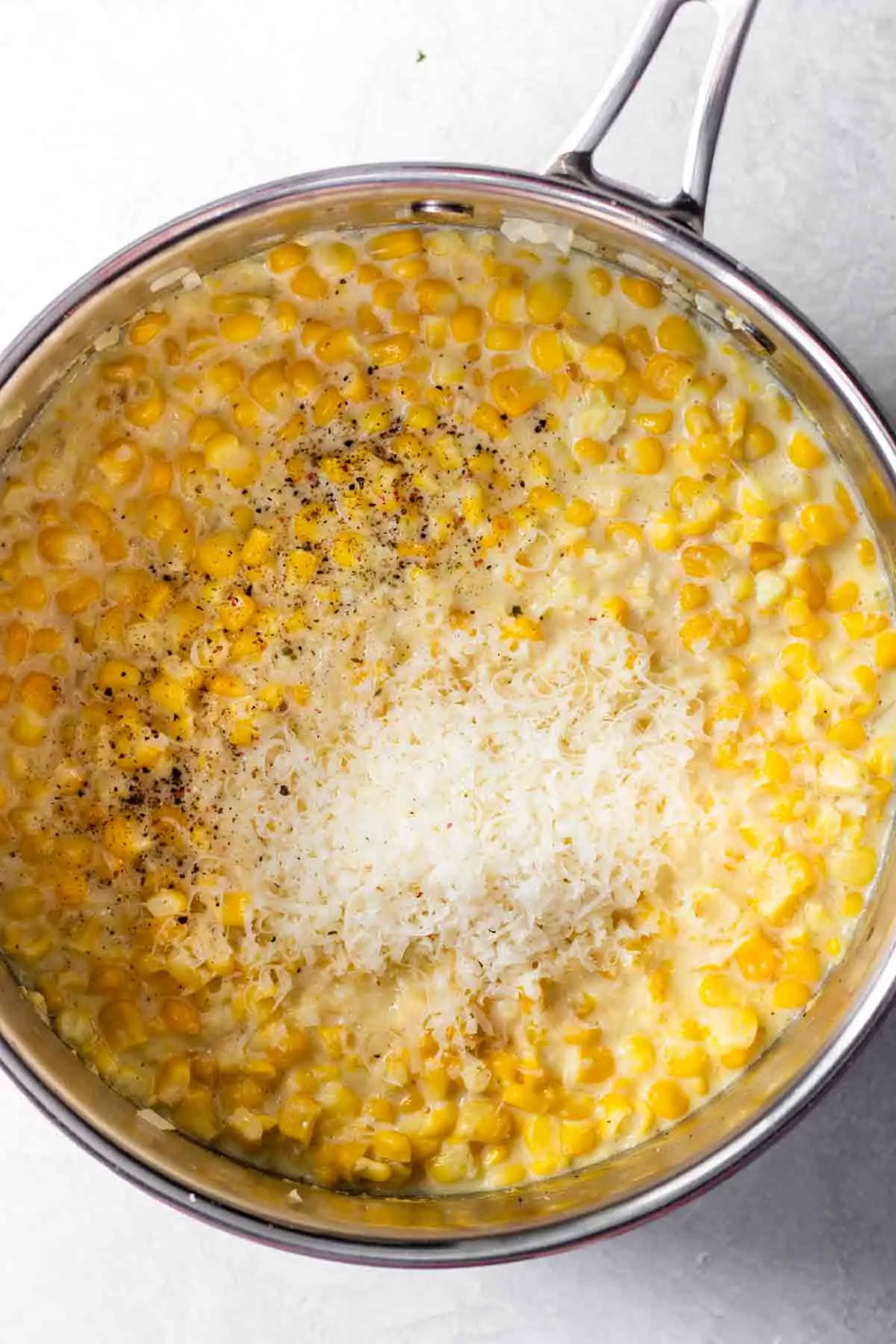 Pot filled with fresh corn, cream, seasonings and parmesan cheese to make homemade creamed corn.