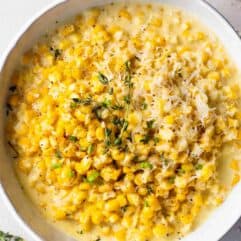 Bowl of creamed corn topped with shredded parmesan cheese and fresh thyme.