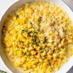 Bowl of creamed corn topped with shredded parmesan cheese and fresh thyme.
