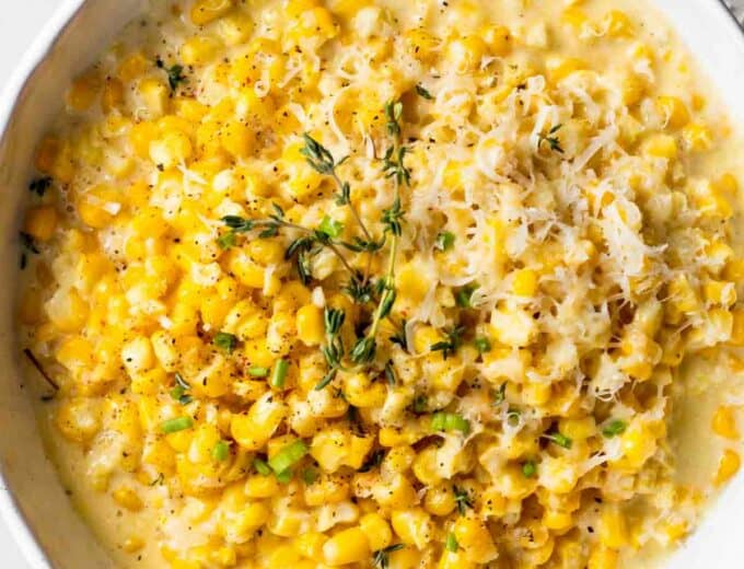 Bowl of creamed corn topped with shredded parmesan cheese and fresh thyme.