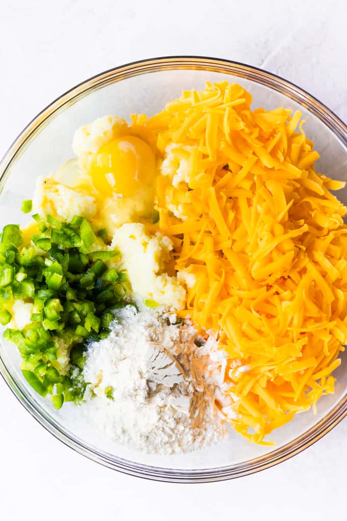 Mixing bowl filled with mashed potatoes, grated cheese, flour, egg, and jalapeno.