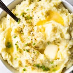 Bowl filled with mashed potatoes topped with melted butter and fresh chives.