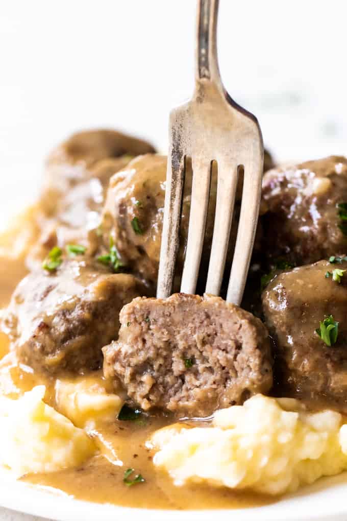 A fork sticking into half of a Swedish meatball showing the texture of the meat inside.