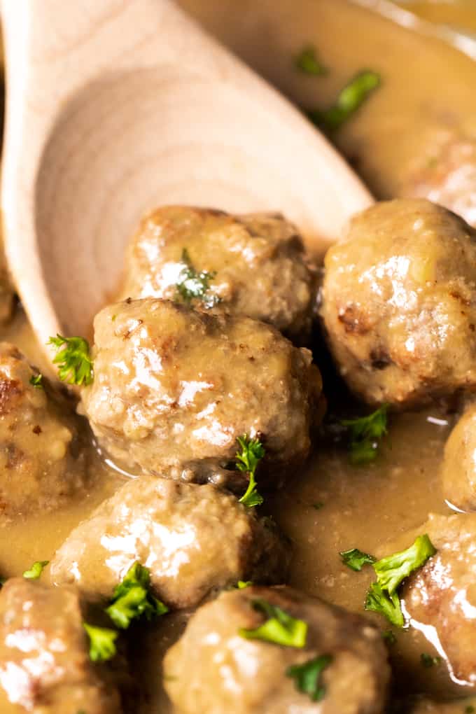Wooden spoon scooping up Swedish meatballs in a creamy gravy. 